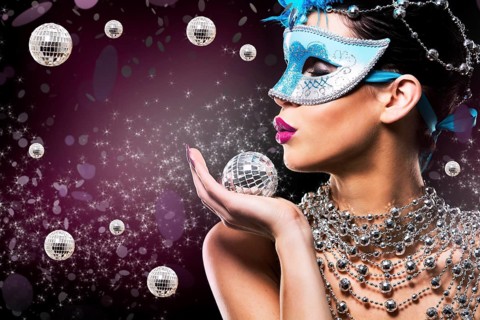 Beautiful woman with dark makeup wearing blue and silver mask surrounded by party accessories on