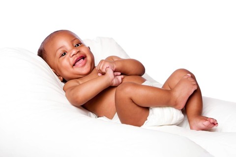 Happy cute smiling laughing African baby infant laying wearing diapers on soft bed, isolated,