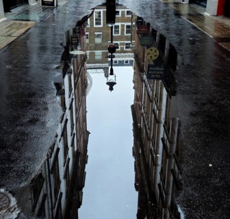 Street scene with puddle reflecting brick buildings and lanterns creates urban and wet ambience,