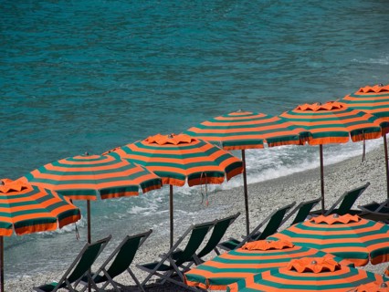 Row of striped parasols on a pebbly beach with a view of the sea and gentle waves, Monte rosso,