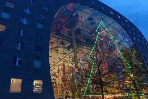 Modern glass façade with large neon-lit Christmas tree decoration at dusk, Rotterdam, Netherlands