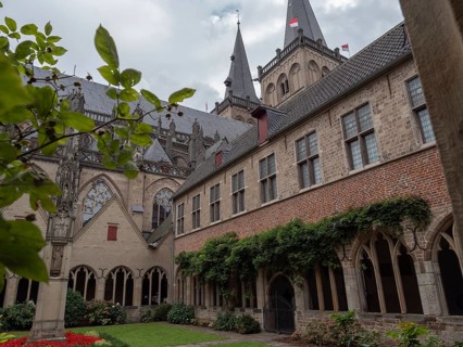 Historic monastery courtyard with Gothic architecture and surrounded by gardens under a cloudy sky,