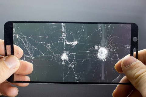 Broken protective glass of smartphone with cracks in hands on black background. Damaged protective