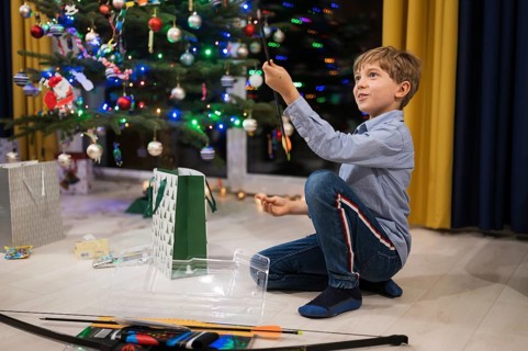 Happy boy opening a Christmas gift and Christmas tree in the background