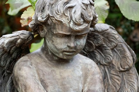 Little angel in a cemetery looks sadly to the ground