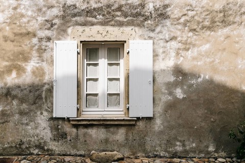 Old window with wooden white painted open shutters in weathered plaster wall