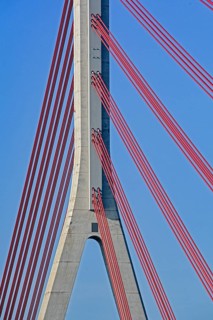 Close-up of red cables supporting a concrete pillar of a modern cable-stayed bridge against a