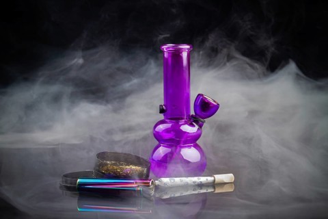 Purple glass bong pipe with joint and a lot of smoke. Cannabis smoker starter pack