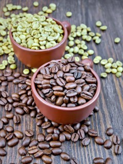 Grains of green and black coffee in brown clay cups and on a table on the background of a wooden