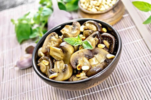 Champignons baked with oregano, wine, garlic, lemon and pine nuts in bowl on background of brown