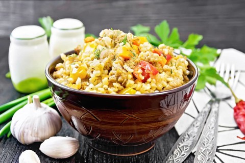 Barley porridge with minced meat, yellow and red bell peppers, garlic and onions in a clay bowl, a