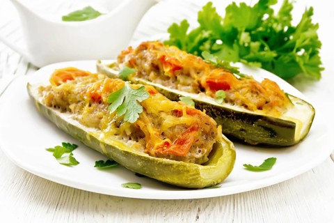 Cucumbers stuffed with minced meat, tomatoes, pepper with cheese and parsley in a plate, cream and