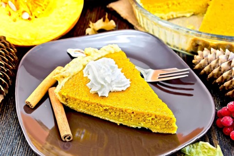 A piece of pumpkin pie with whipped cream in a brown plate with a fork and cinnamon, pumpkin,
