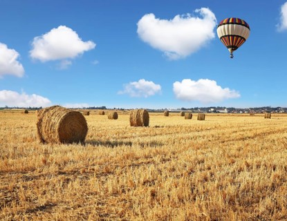 Red and blue balloon slowly floating over kibbutz field. Stacks of harvested wheat beautifully and