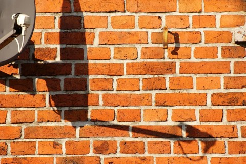 A satellite dish on a brick building casts a shadow