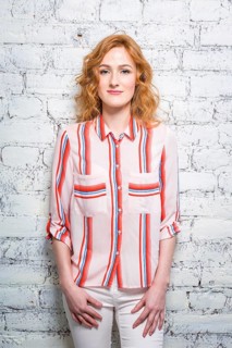 A beautiful young woman student with red curly hair and freckles is leaning against a brick wall of