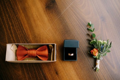 Accessories for the groom bow tie, gold wedding ring and boutonniere on a wooden floor in a row.