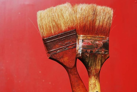 Closeup of two dirty paintbrushes against red background