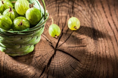 Fresh gooseberries in basket on vintage wooden board