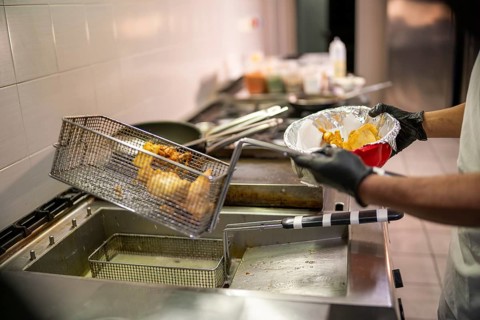 Someone is deep frying food in a professional kitchen with a fryer and metal basket