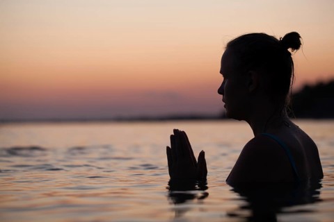 Woman in sea water at sunset alone. She praying or meditating