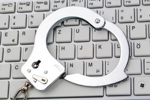 Handcuffs lying on the keyboard of a computer. Symbolic photo for criminality, computer crime and
