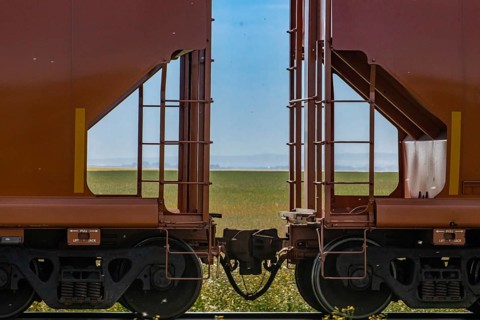 Close up of train coupler connecting two red wagons of a Canadian freight or cargo train. Green