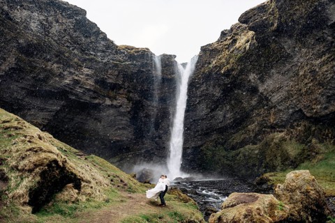 The groom circles the bride in his arms near the waterfall, it is snowing. Destination Iceland