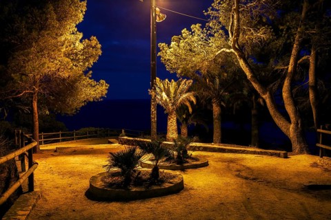 Gloomy square in abandonded park by the sea at midnight illuminated by single lamp, Costa Brava in