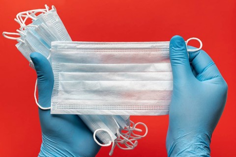 Doctor holds lot respiratory surgical face mask in hands blue medical gloves on red background.