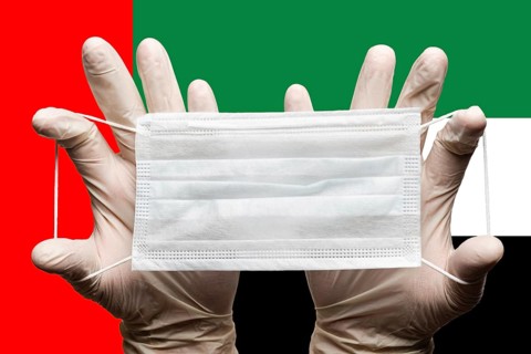 Medic holds protective respiratory face mask in two hands in white gloves on background of national