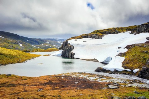 The cold water of the lake is covered with ice floes. Gorgeous Snow Road in Norway. Cold July in