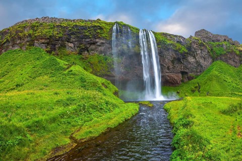 The warm July day in Iceland. Seljalandsfoss waterfall. Rainbow decorates drop of water