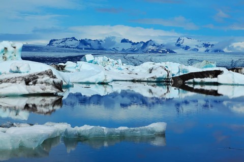 Sunrise. Blue and emerald icebergs and ice floes are reflected in smooth water of the Gulf