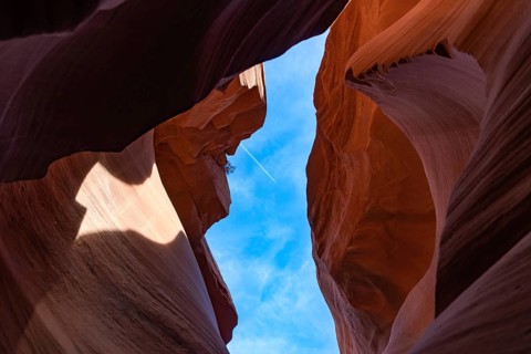 A picture of the rock formations of the Lower Antelope Canyon, while a plane is flying in the blue