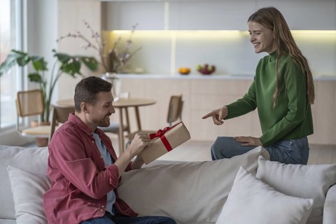 Happy couple celebration. Loving pleased woman gives gift with red tape to smiling husband.