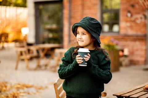 Cute little girl drinking hot cocoa from paper cup in outdoor cafe or backyard. Autumn concept