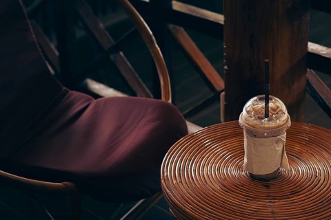 A cozy cafe setting with an iced coffee on a round rattan table and chair