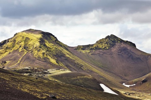 National Park Landmannalaugar in July. Green and pink mountain slopes and snowy white residues from