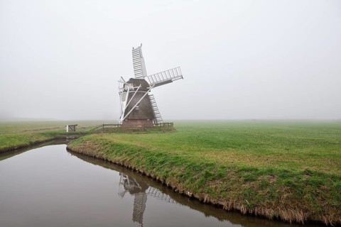 Dutch wooden windmill in fog by canal