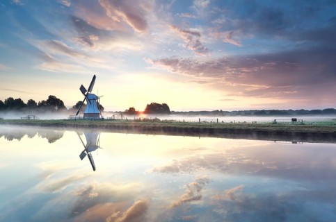 Golden sunrise over windmill reflected in river, Netherlands