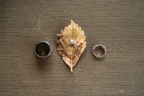 Wedding rings and bride's engagement ring on gray texture with yellow leaf of wood.