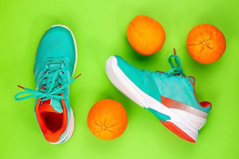 Red, cyan, white pair of new tennis shoes in studio shot over green background with oranges next to