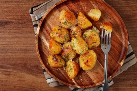 Half-eaten fried new potatoes, with butter and dill, on a wooden plate, with a fork, at home,