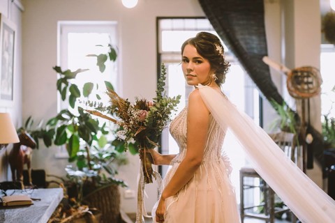 Stylish bride posing at window in light on background. rustic wedding concept. happy bohemian