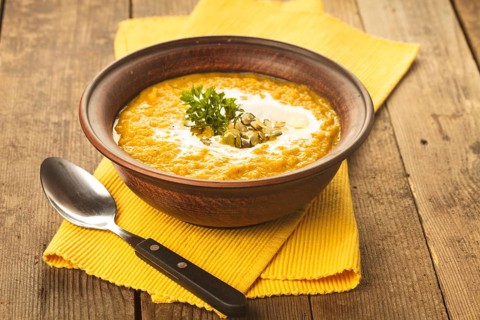 Pumpkin soup in clay bowl with spoon on the table
