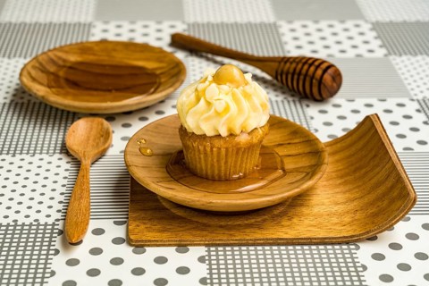 Cupcake and natural honey in a wooden plate with wooden spoon and wooden honey dipper stick