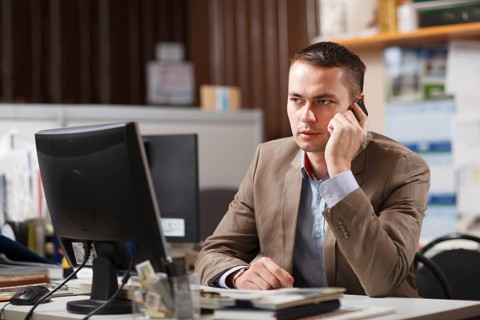 Businessman sitting behind his desk in the office talking on a mobile phone listening to the