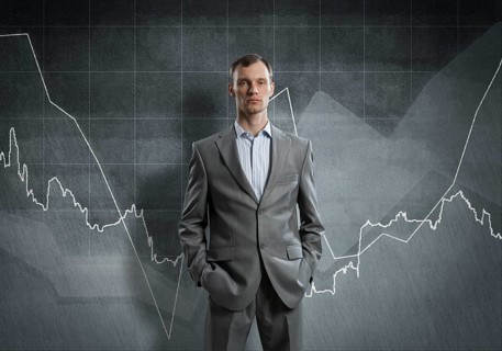 Businessman with arms in pockets and growing graphs on chalkboard