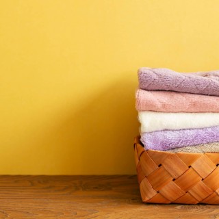 Stack of bath towels in basket on wooden table. yellow background. copy space